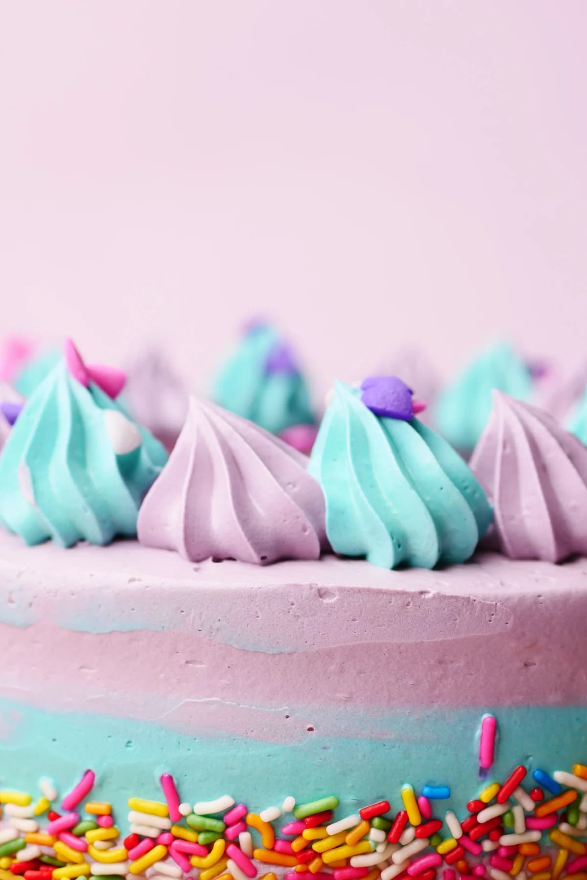 Pink cake topped with blue and lilac piped frosting and colorful sprinkles