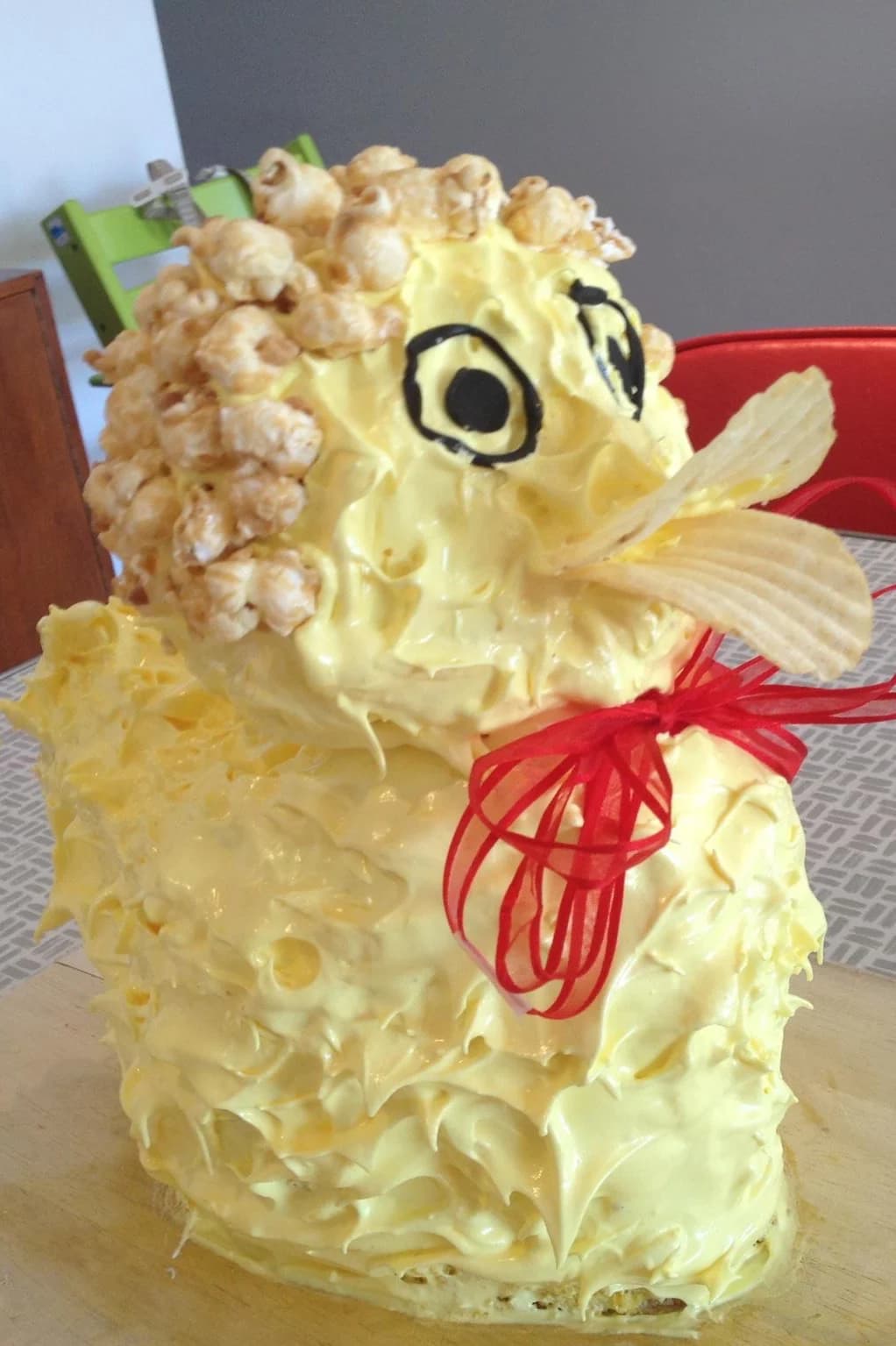 A yellow duck-shaped cake with orange beak, large eyes and a ribbon