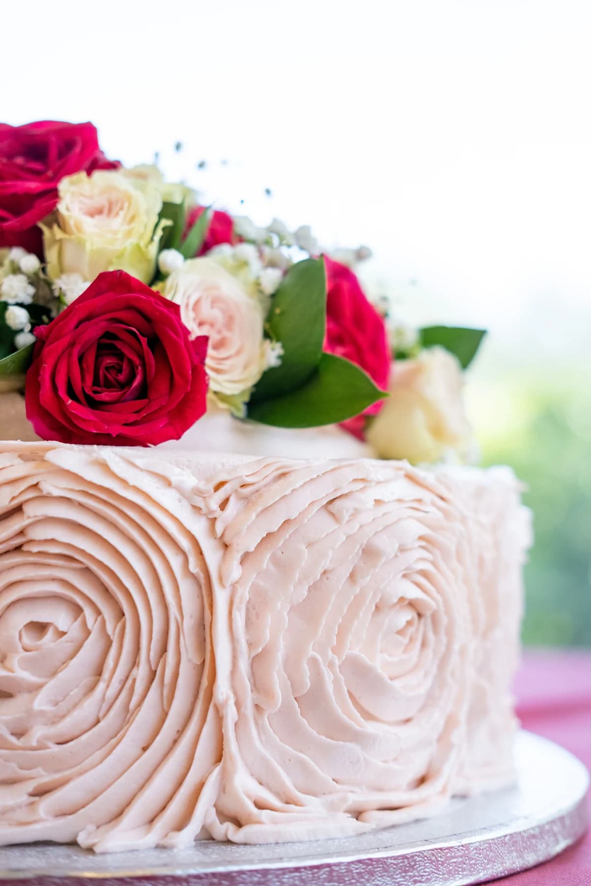 White rosette-covered cake with roses arranged on top