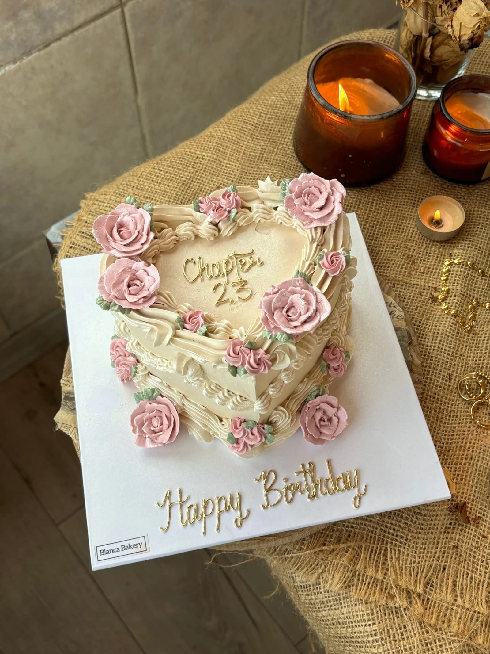 Ivory heart-shaped cake with pink roses, shell borders, hanging swags and gold-colored birthday lettering.
