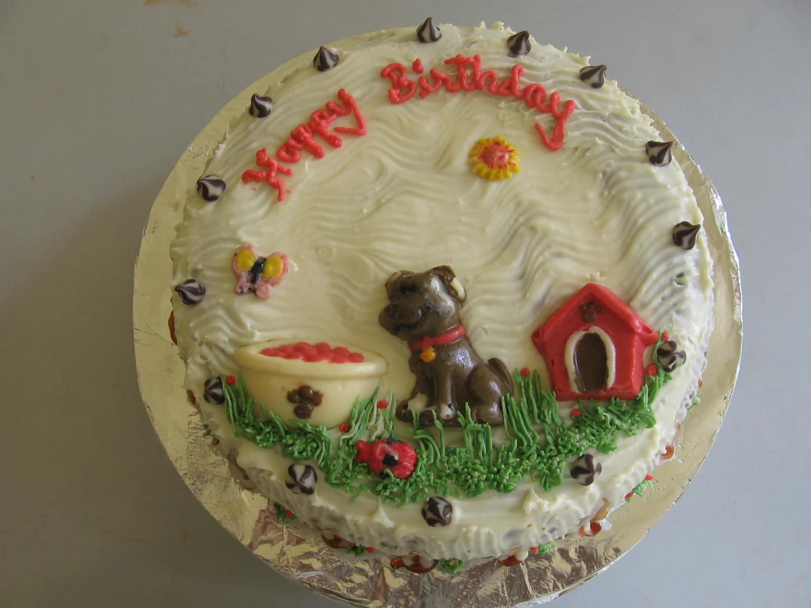 White birthday cake with a small dog figure, doghouse and piped flowers