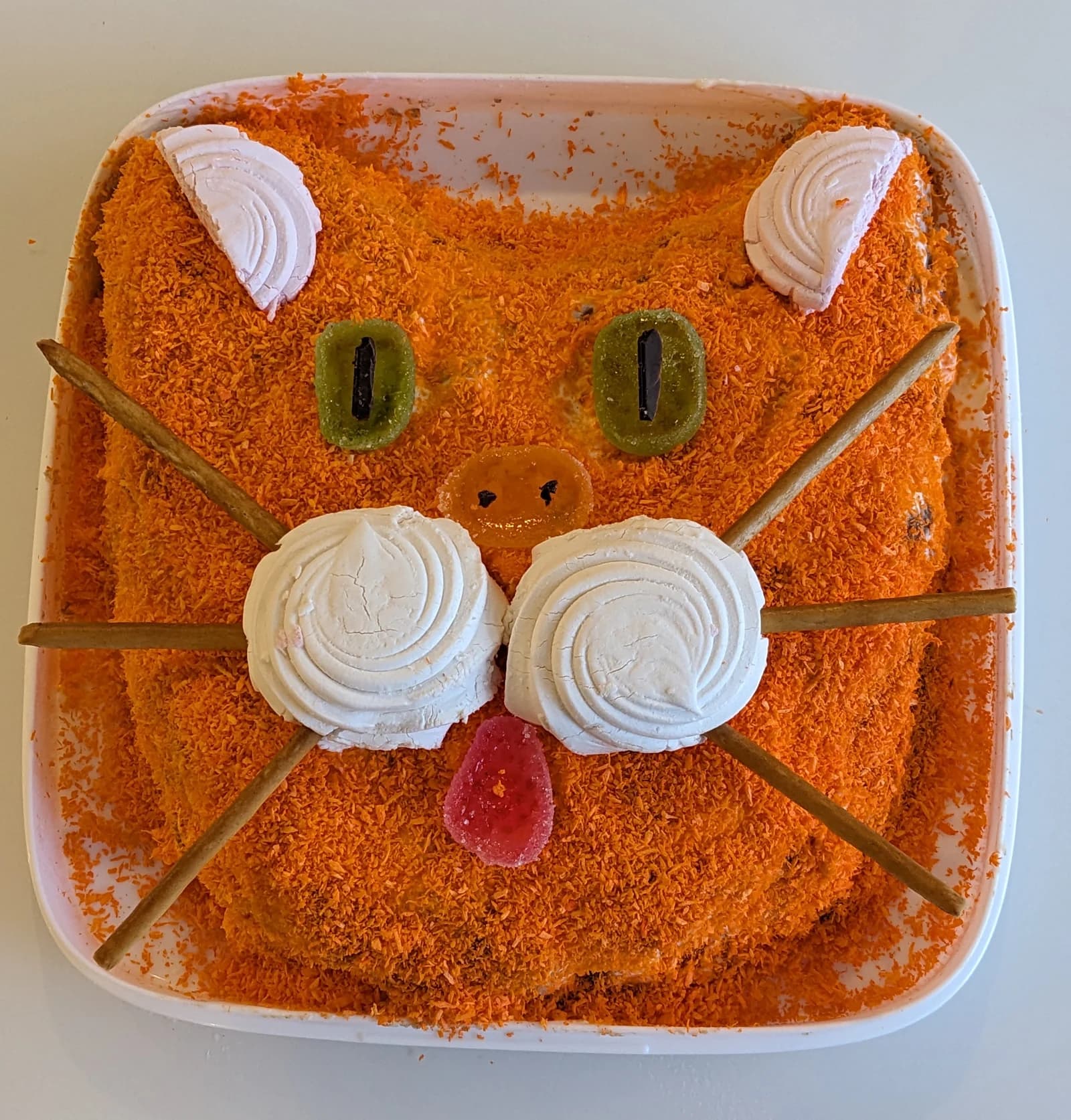 A square orange cat-face cake with whiskers and a piped white muzzle