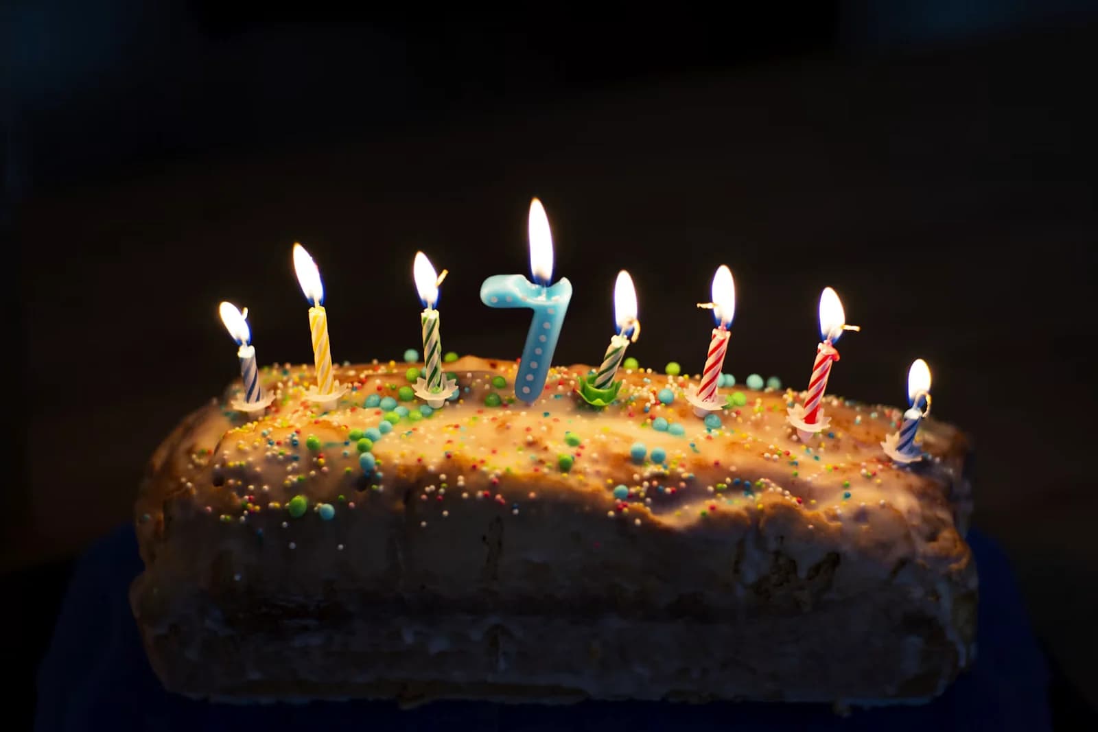 A rectangular birthday cake with colorful sprinkles and lit candles