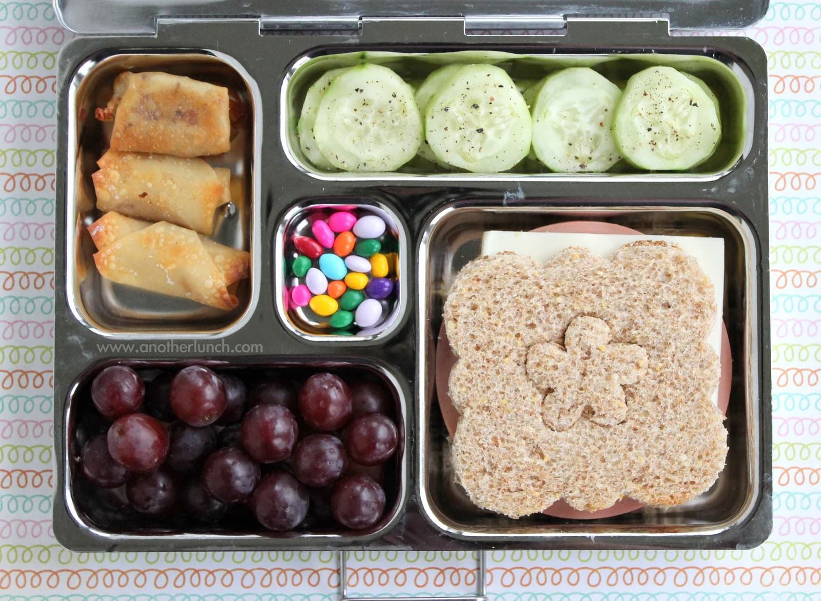 A lunch box containing a flower-shaped sandwich, grapes and vegetables