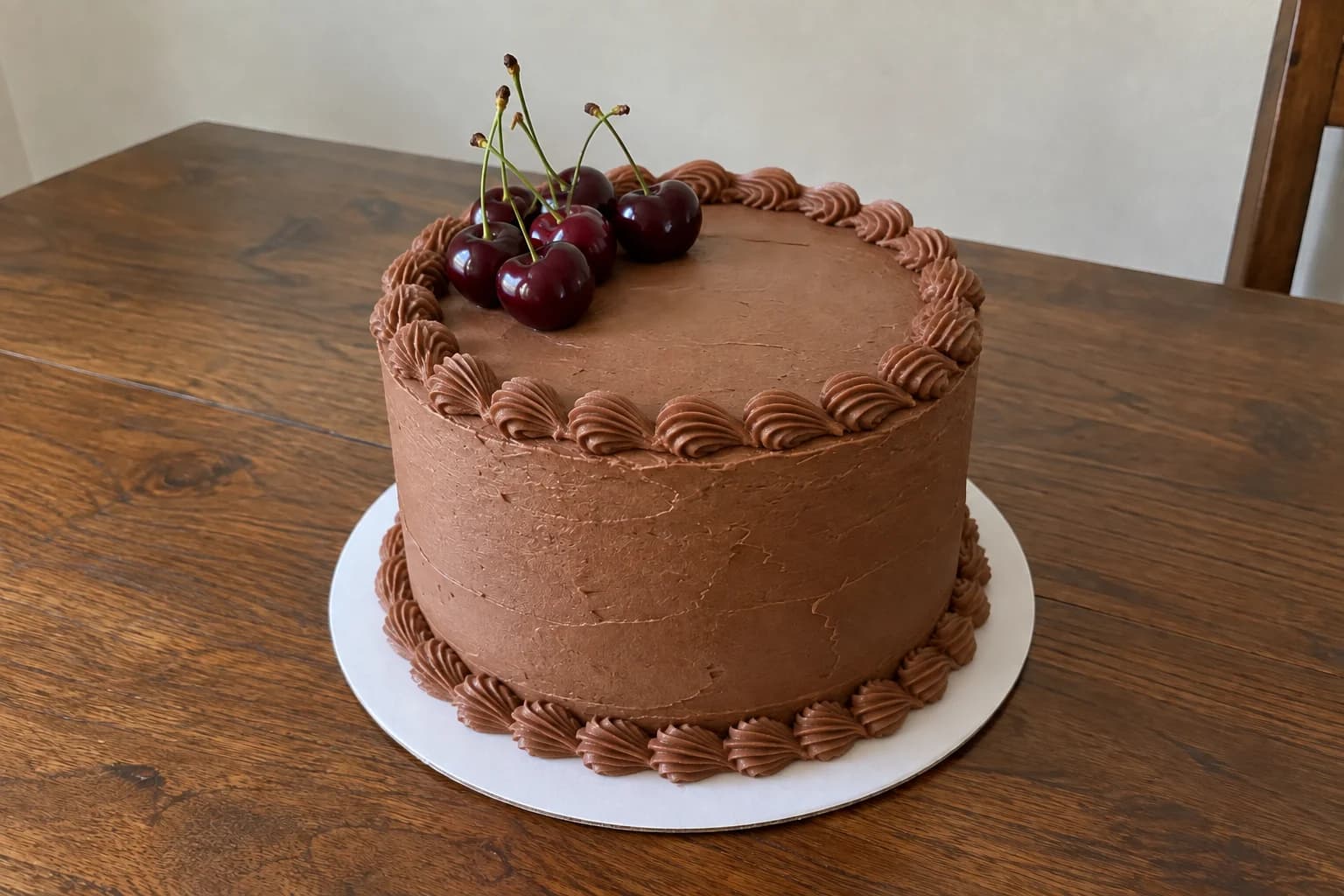 AI illustration of a chocolate cake with piped shell borders around the top and base, finished with dark cherries on a white board.