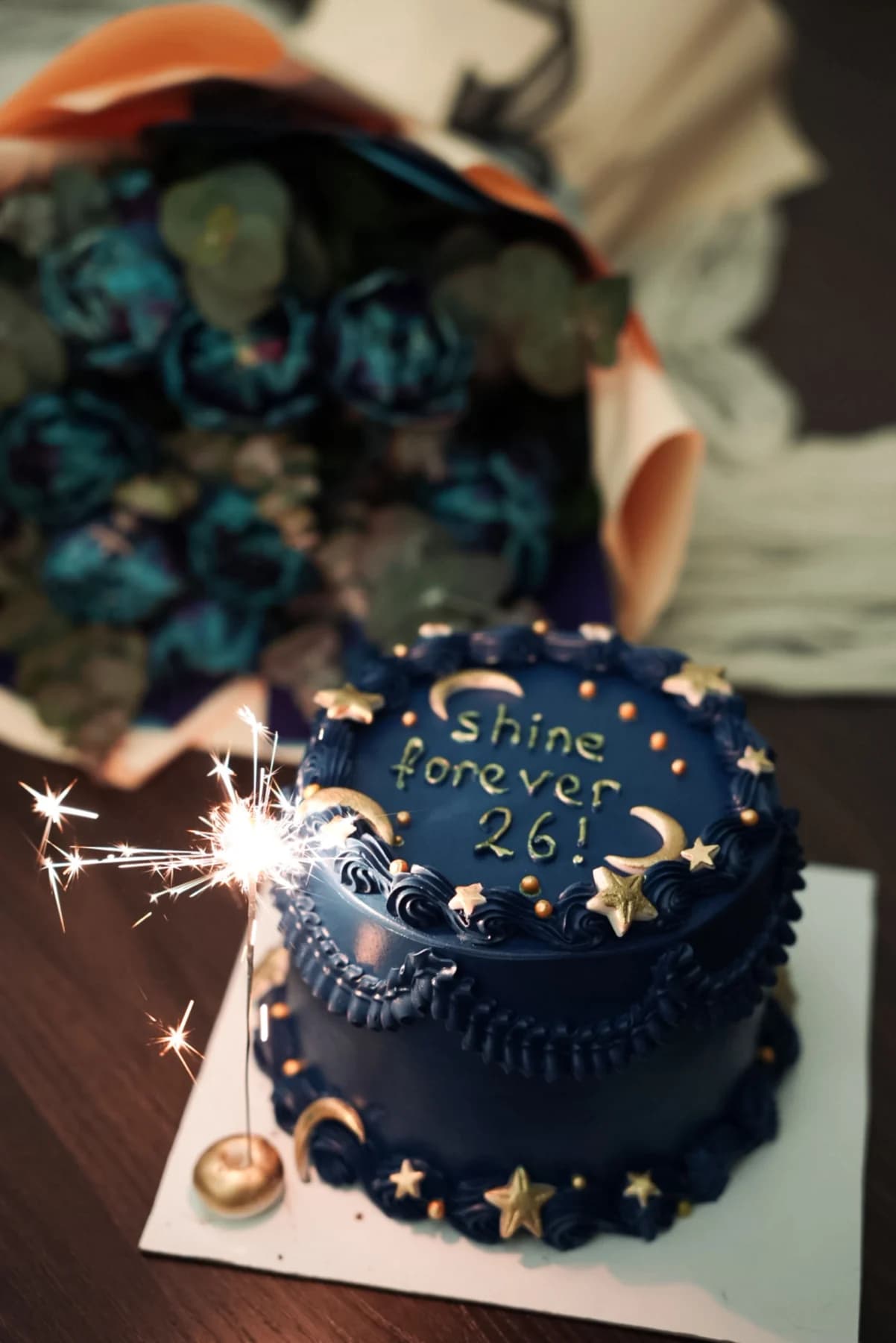 Dark blue birthday cake with moon and star decorations and a lit sparkler