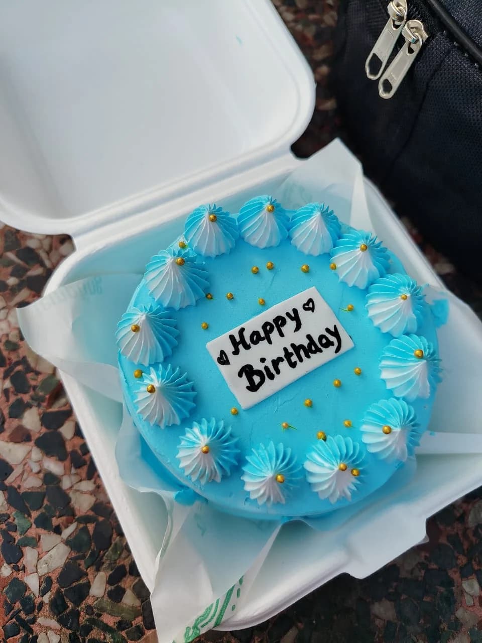 Blue-frosted mini cake with piped borders in a takeaway box