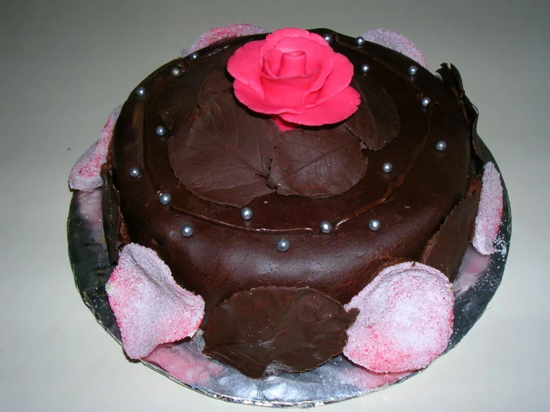 Dark chocolate cake decorated with a pink rose and chocolate leaves
