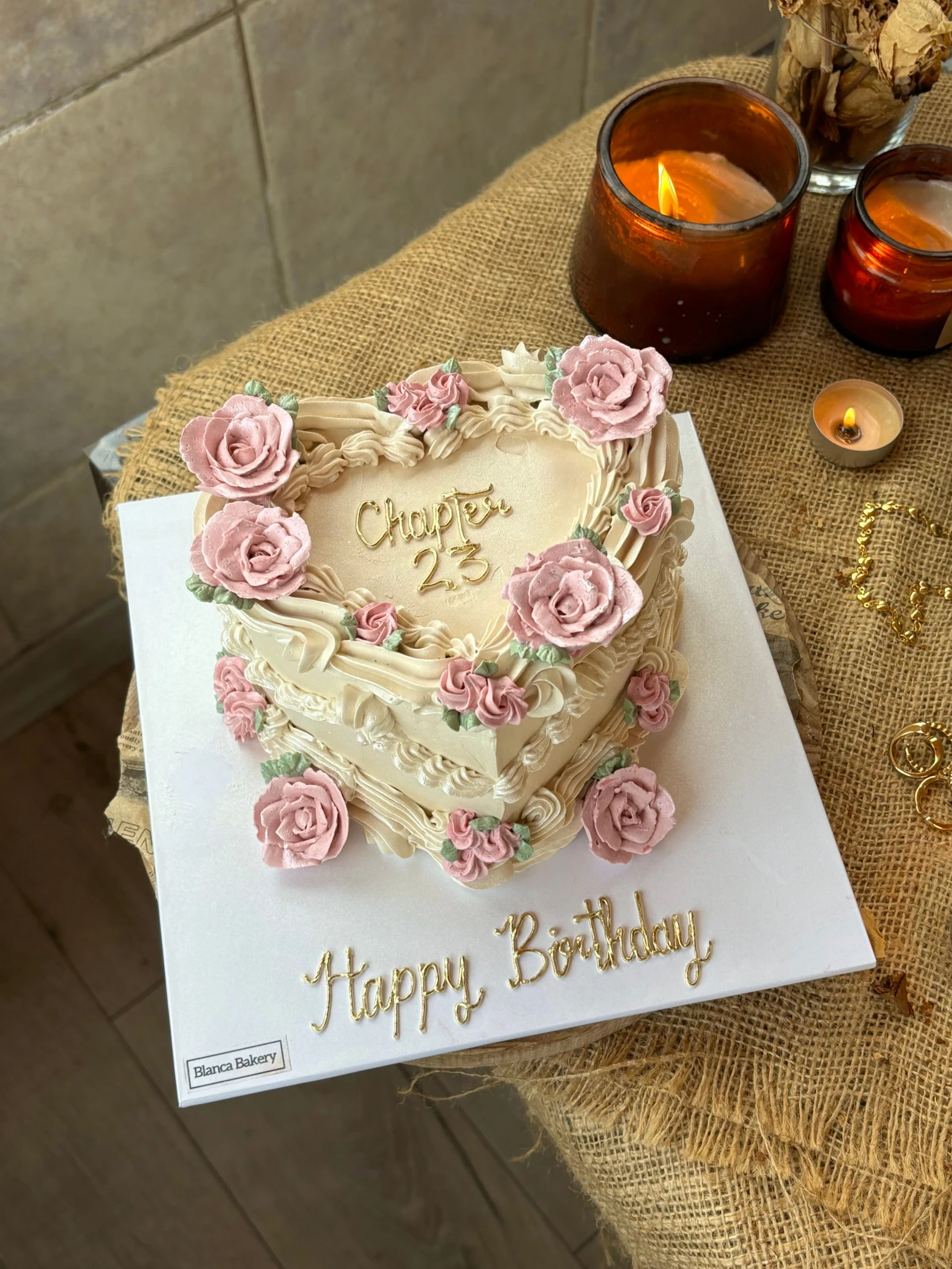 Ivory heart-shaped cake with pink roses, shell borders, hanging swags and gold-colored birthday lettering.