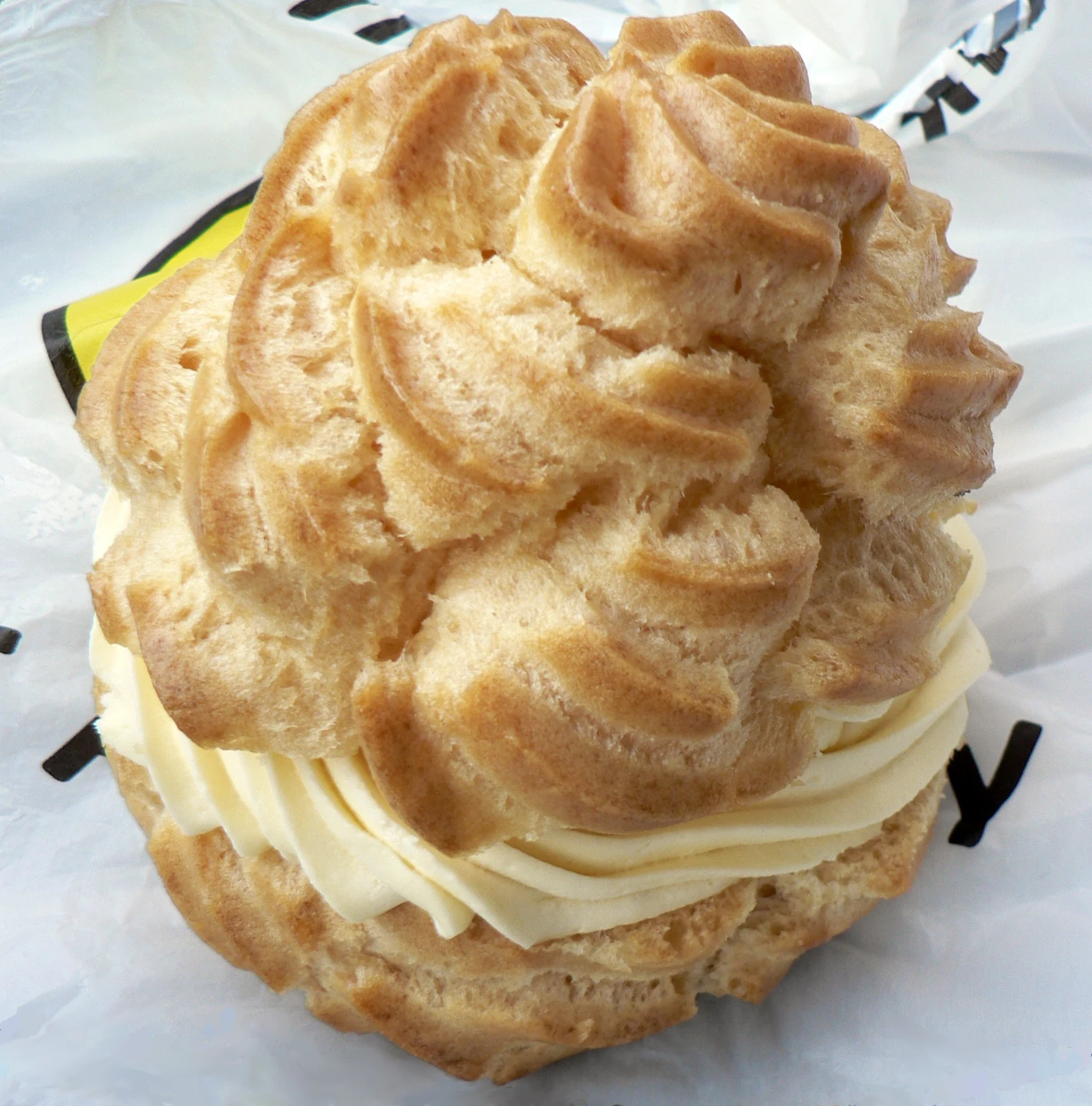 Close-up of a large round cream puff made from golden-brown ridged choux shells, with a thick layer of pale piped cream between them.