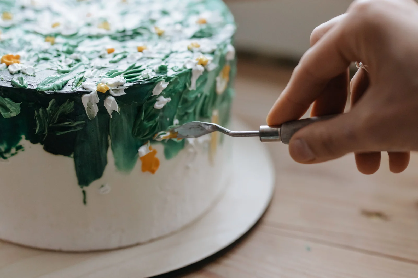 A palette knife spreading green icing on the side of a white cake