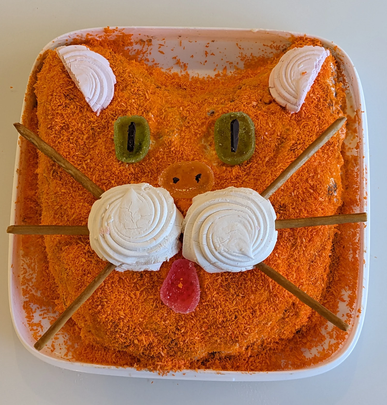 A square orange cat-face cake with whiskers and a piped white muzzle