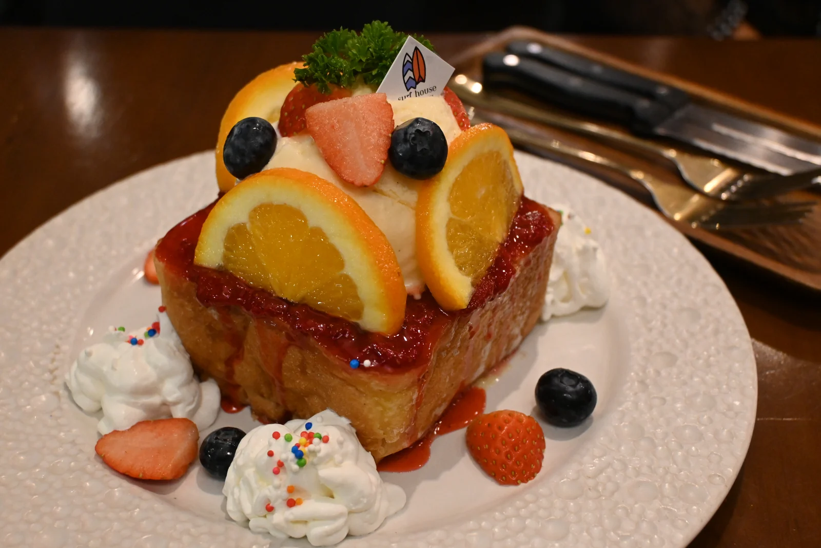 Thick toast with whipped cream, orange slices, berries and strawberry sauce