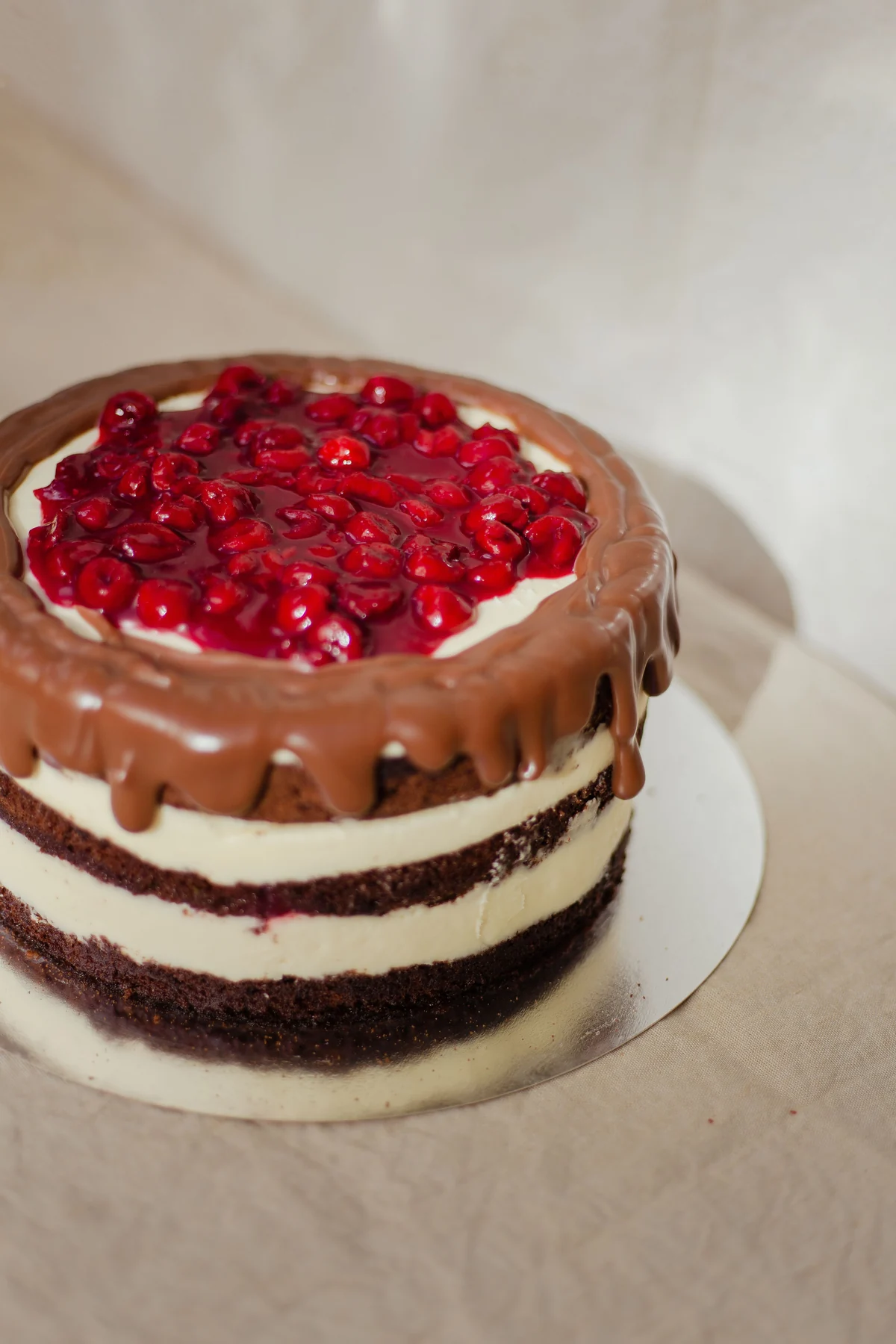 Chocolate layer cake with cream filling, chocolate drips and red cherries
