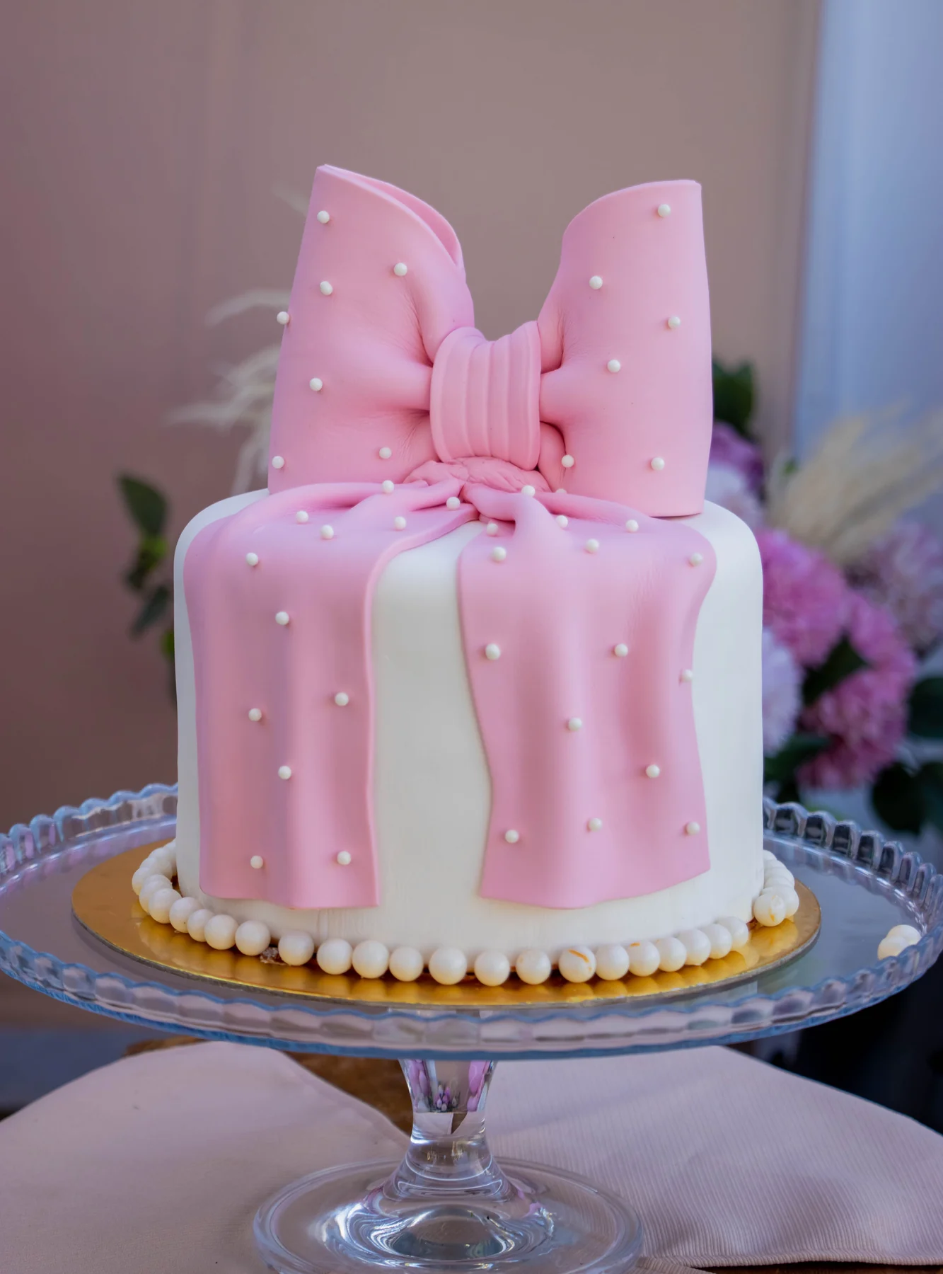 White cake with a large pink fondant bow, white pearls and a piped pearl border